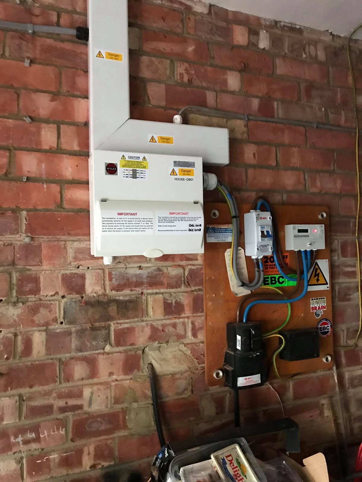 A Wylex consumer unit with trunking and meter tails, fitted on a brick wall
