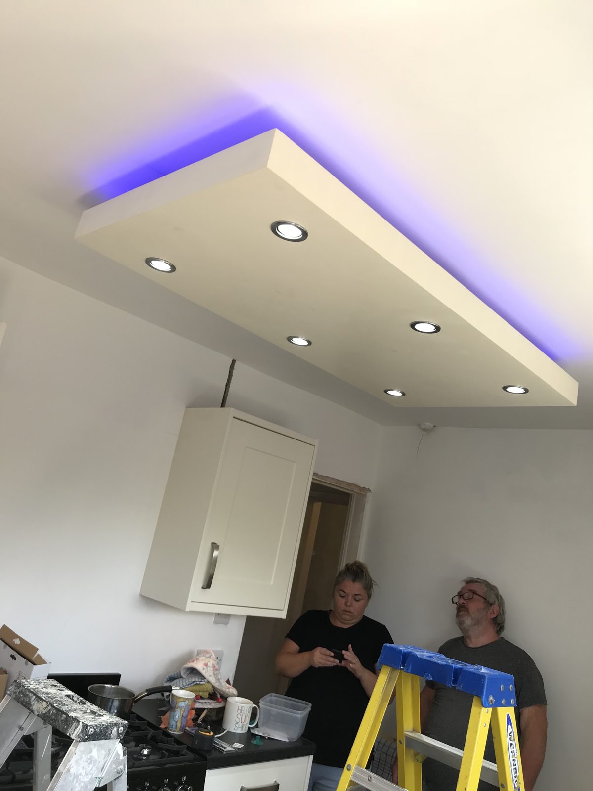 A floating ceiling panel with recessed spotlights and blue LED edge lighting in a kitchen